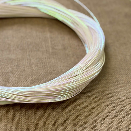 Pearl Aurora foil-wrapped Japanese mizuhiki cord looped on a textured beige fabric background