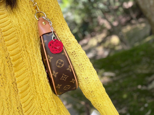 Red handmade mizuhiki bag charm attached to a monogram bag beside a mustard knit cardigan in Kyoto